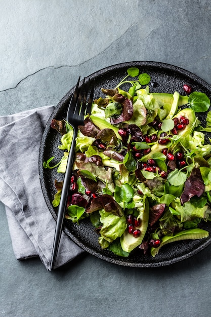 Lettuce salad with pomegranate on black plate. Top view