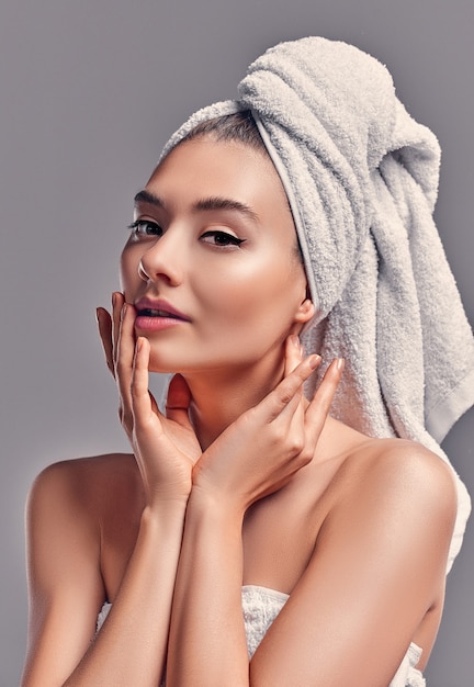 Leuk aantrekkelijk meisje met handdoek op haar hoofd geïsoleerd op een grijze achtergrond. Huidverzorgingsconcept. Spa-behandelingen, cosmetologie, make-up.