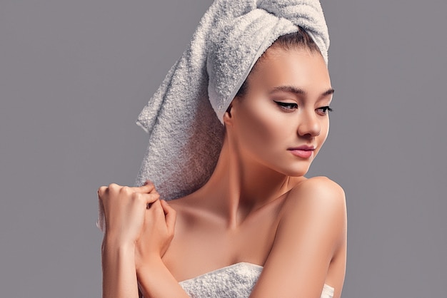 Leuk aantrekkelijk meisje met handdoek op haar hoofd geïsoleerd op een grijze achtergrond. Huidverzorgingsconcept.