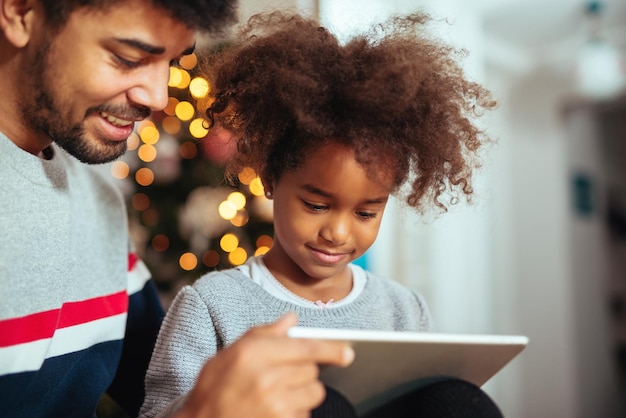 Leuk Afrikaans Amerikaans meisje dat thuis tablet met papa gebruikt