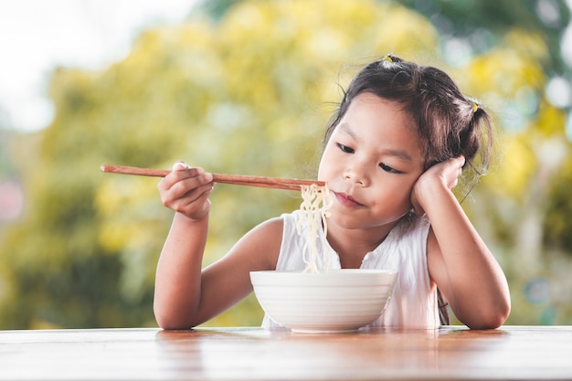 Leuk Aziatisch kindmeisje bored om Onmiddellijke noedels voor haar maaltijd te eten