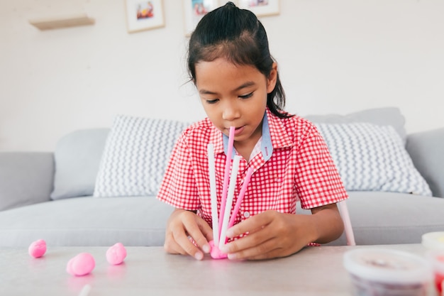 Leuk Aziatisch kindmeisje dat speelt en creëert met speeldeeg en rietjes. Kind geconcentreerd met playdough bouwen van een molecuulmodel. Kid en ambacht met recycle dingen.