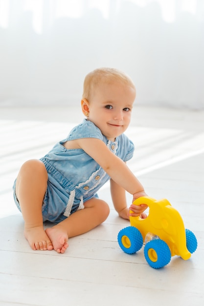 Leuk babymeisje die in blauw kostuum gele olifant met wielen houden