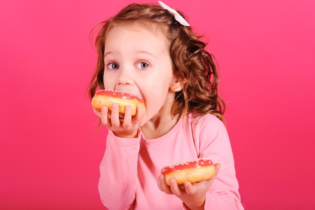 Leuk babymeisje die zoete donuts over roze achtergrond eten