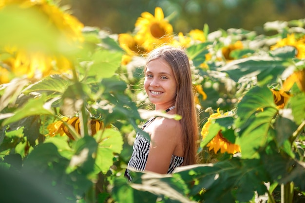 Leuk blank tienermeisje dat lacht in een veld met zonnebloemen. Zomertijd concept.