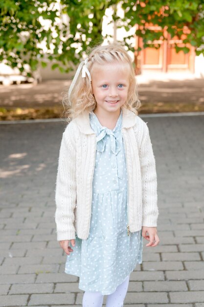 Foto leuk blond meisje met een jurk in pastelkleuren tegen de achtergrond van het park