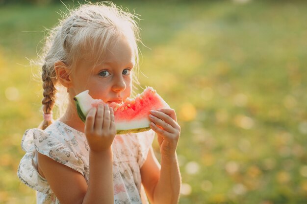 Leuk blond meisje met watermeloen op het gras in park.