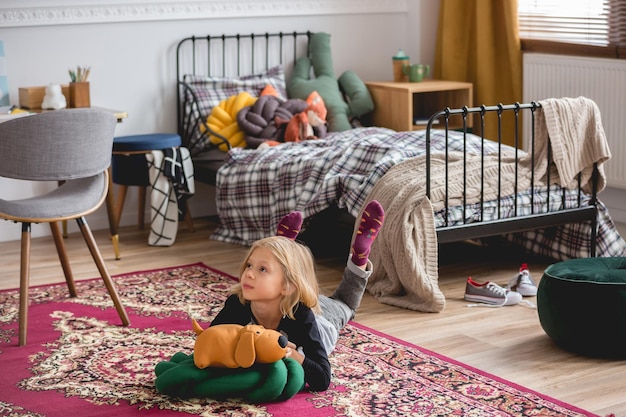 Leuk blond meisje op de vloer van de trendy kinderkamer die met haar speelgoed speelt.