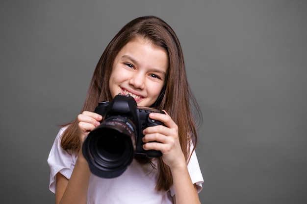 Leuk bruin meisje met een fotocamera geïsoleerd op een grijze achtergrond