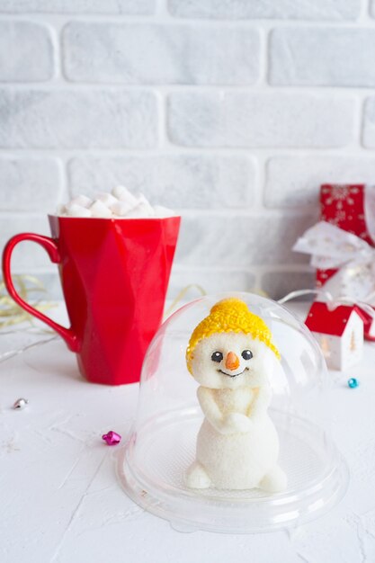 Leuk chocolade sneeuwpop beeldje in plastic verpakking. rode mok met koffie en marshmallows en een rode geschenkdoos.