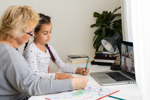 Leuk en gelukkig klein meisje dat een laptopcomputer met haar oma gebruikt, studerend via een online e-learningsysteem.