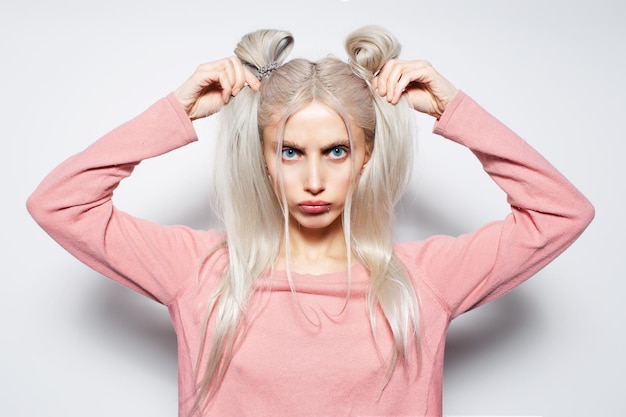 Leuk en grappig blond meisje dat haar haarbroodjes vasthoudt op een witte studioachtergrond