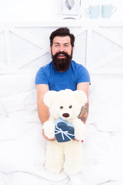 Leuk en romantisch cadeau bebaarde hipster bereidt een mooi cadeau voor valentijnsdag cadeau verspreid liefde cadeau voor lieverd man knuffel zacht stuk speelgoed ontspannen in bed maak verrassingsconcept cadeau voor echtgenoot