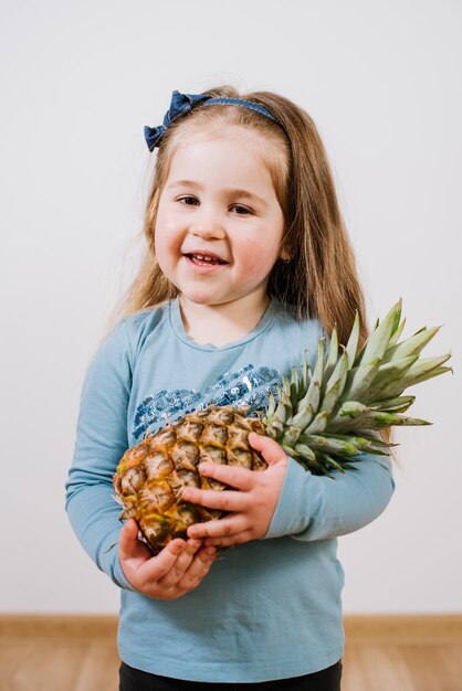 Leuk gelukkig meisje dat een ananas op grijze achtergrond houdt