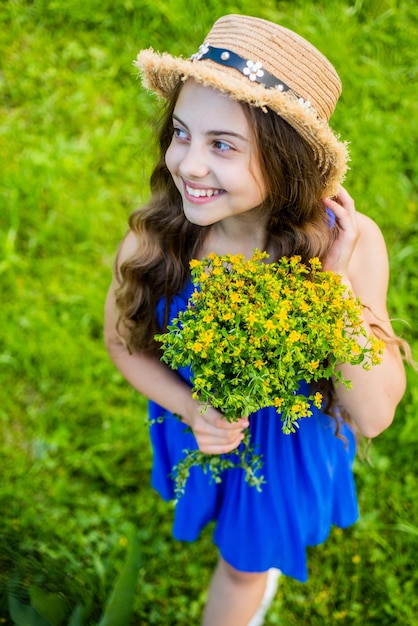 Leuk glimlachend meisje dat strohoed draagt die gele bloemen in veld verzamelt