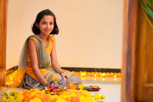 Leuk indisch meisje dat decoratie maakt met bloem en olielamp voor diwali-festival thuis