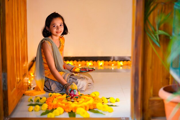 Leuk indisch meisje dat decoratie maakt met bloem en olielamp voor diwali-festival thuis