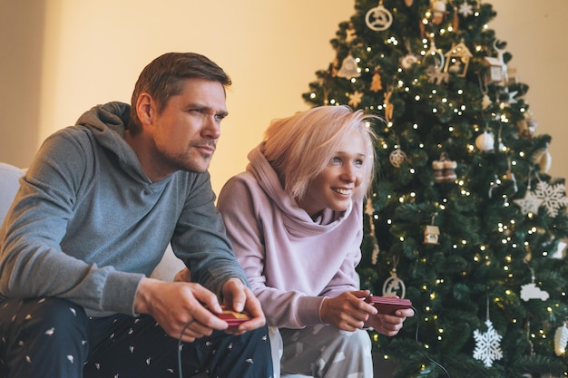 Leuk jong gezin in huiskleding die videogames speelt op de bank op de achtergrond van de kerstboom