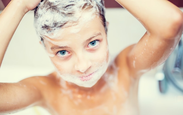 Leuk jong meisje in douche wassen haar en gezicht met shampoo.