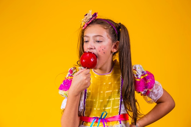 Leuk Kaukasisch meisje in typische festa junina-outfit die appel met karamel eet