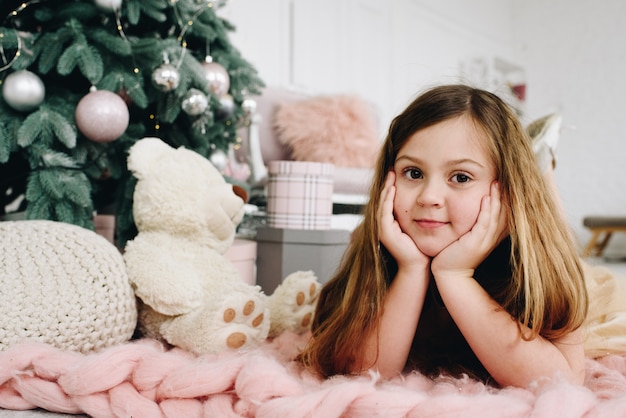 Leuk Kaukasisch schoolmeisje dat dichtbij haar speelgoed en verfraaide Kerstboom ligt