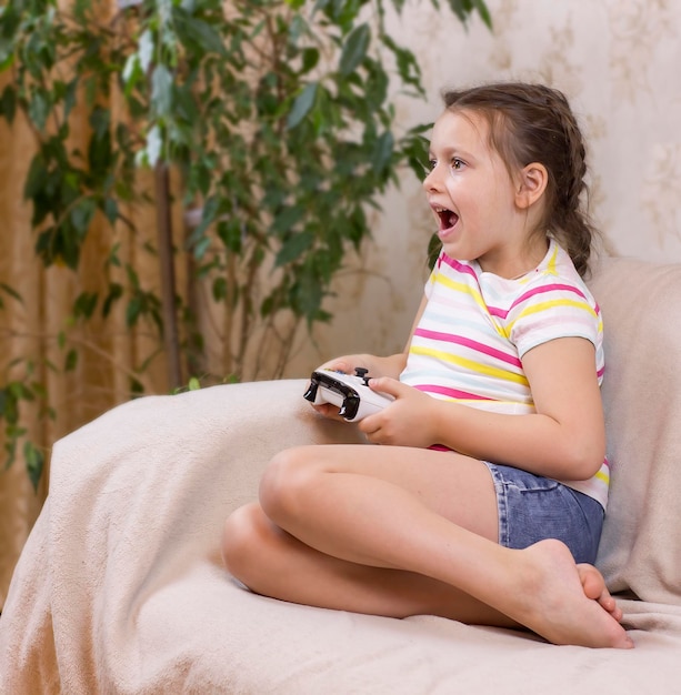 Leuk kindmeisje dat een joystick vasthoudt en thuis een videogame speelt op een bank