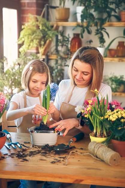 Leuk kindmeisje helpt haar moeder om voor planten te zorgen. moeder en haar dochter houden zich bezig met tuinieren. gelukkige familie in de lentedag.