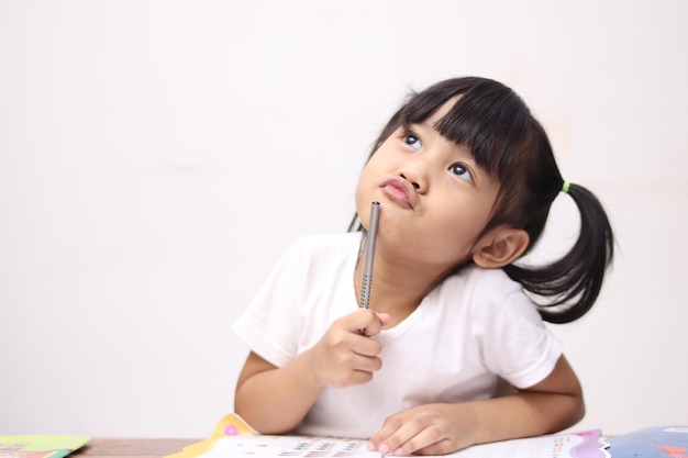 Leuk klein Aziatisch baby meisje houdt pen boek leren terwijl je aan iets denkt goed idee glimlachend