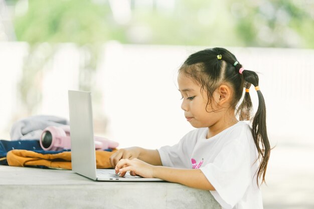 Leuk klein Aziatisch meisje met een laptop in het openluchtpark.