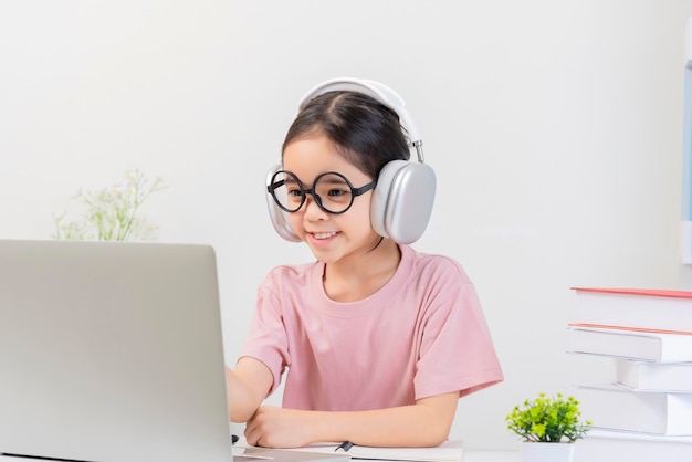 Leuk klein Aziatisch meisje studeert thuis met laptop en draadloze koptelefoon.