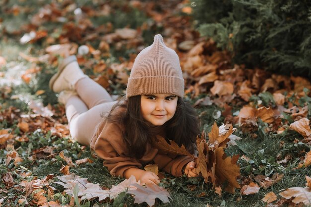 Leuk klein brunette meisje dat in de herfst op het gras ligt.