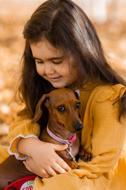 Foto leuk klein brunette meisje loopt in de herfst met een dachshund hond in het park