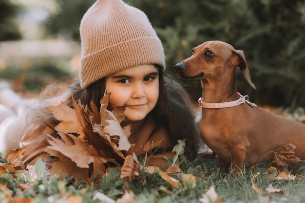 Foto leuk klein brunette meisje loopt in de herfst met een dachshund hond in het park