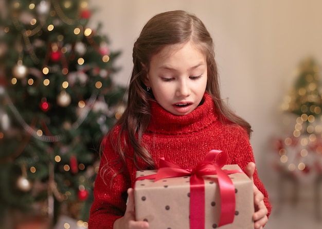 Leuk klein kindmeisje met huidige giftdoos dichtbij Kerstboom thuis.