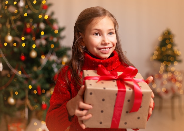 Leuk klein kindmeisje met huidige giftdoos dichtbij Kerstboom thuis.