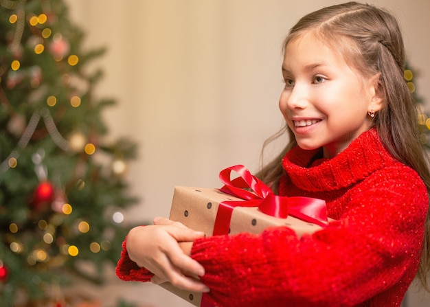 Leuk klein kindmeisje met huidige giftdoos dichtbij Kerstboom thuis.