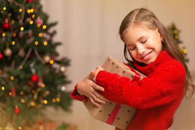 Leuk klein kindmeisje met huidige giftdoos dichtbij Kerstboom thuis.