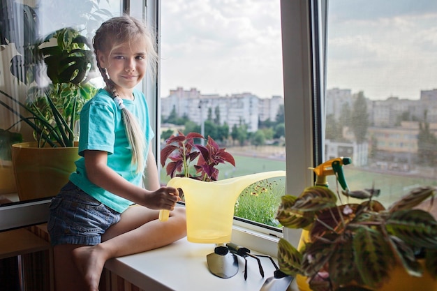 Leuk meisje dat helpt bij het verzorgen van huisplanten op het balkonraamconcept van de plantenouders