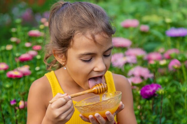 Foto leuk meisje dat honing eet tegen planten.