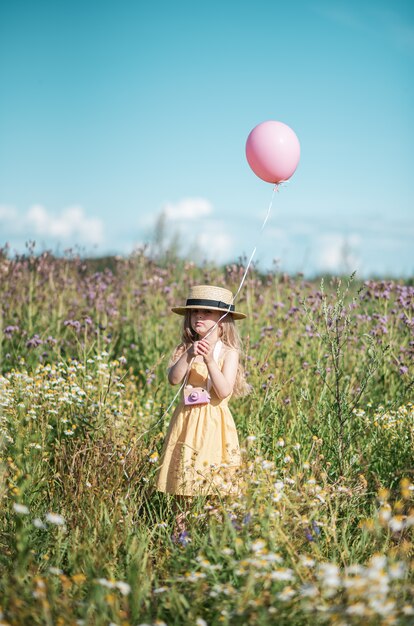 Leuk meisje dat op het bloemengebied loopt in gele kleding en hoed, de zomertijd