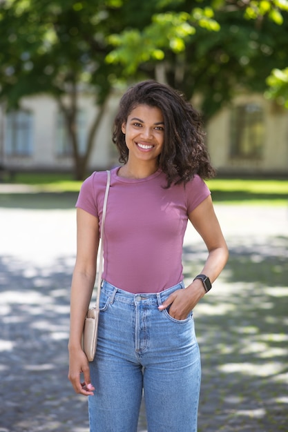 Leuk meisje. Glimlachende schattige mulatta in jeans en roze t-shirt in het park