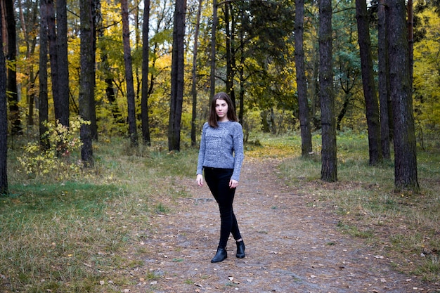 Leuk meisje in een grijze sweater met steunen op haar tanden die zich op de weg in het de herfstbos bevinden