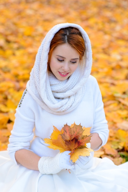 Leuk meisje in lange witte trouwjurk poseren in landelijke pad onder herfst bomen in bos in gouden uur sfeer.
