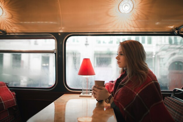 Leuk meisje in plaid zit in een gezellig café met een kop warme drank in haar hand