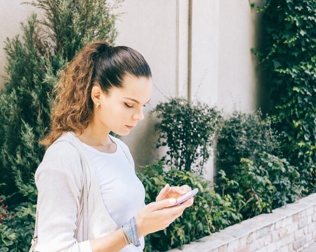 Leuk meisje in wit vest met behulp van een mobiele telefoon buitenshuis