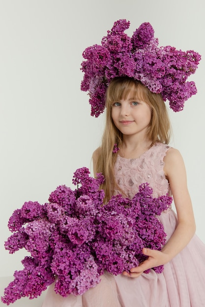 Leuk meisje met blond haar in een roze jurk met een boeket seringen op een witte achtergrond