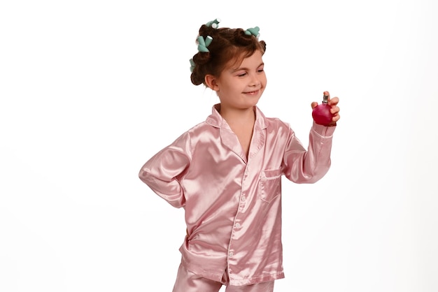 Leuk meisje met krullen in roze zijden pyjama op een witte achtergrond draagt parfum