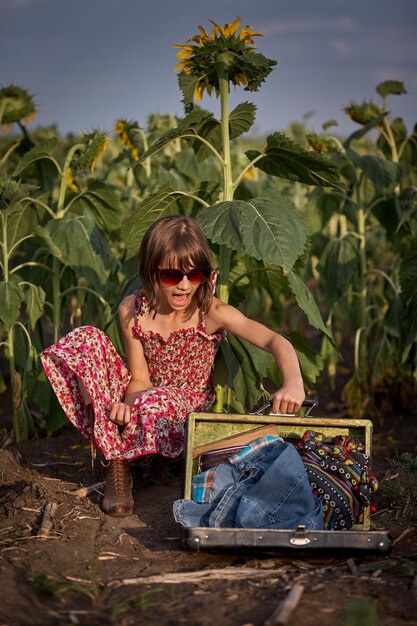 Leuk meisje met oude koffer in een zonnebloemveld