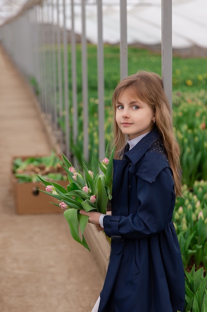 Leuk meisje met tulpen met blond haar voorjaar in een kas met groeiende tulpen