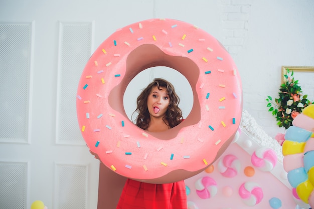 Leuk meisje poseren met roze donuts, gek rond, dessert, slecht eten, kijkt in het gat in de donut, houdt donuts bij de ogen